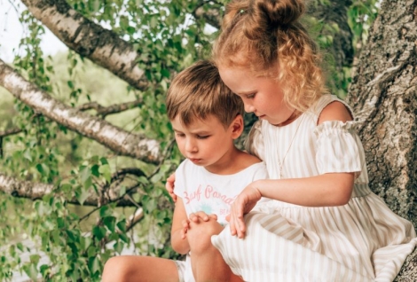 Little sister and brother are sitting on a tree on a summer day.Summer concept.