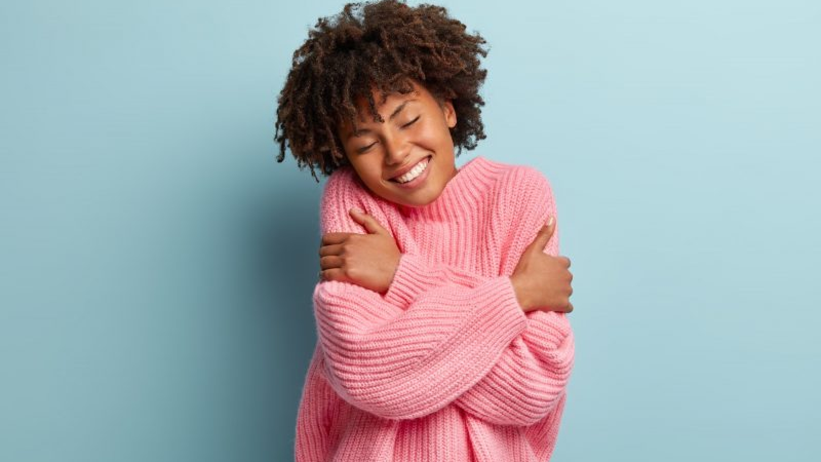 Love yourself concept. Photo of lovely smiling woman embraces herself, has high self esteem, closes