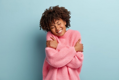 Love yourself concept. Photo of lovely smiling woman embraces herself, has high self esteem, closes