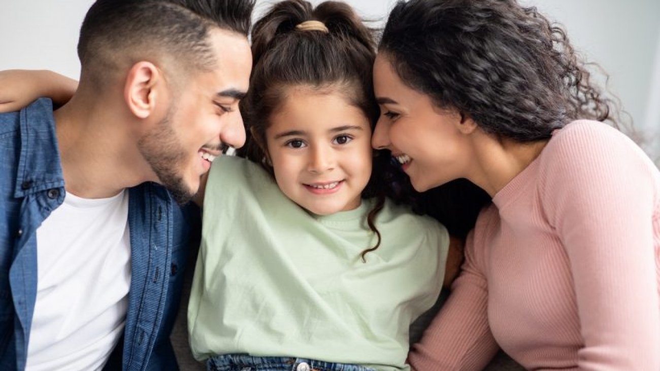 Parental Love. Happy Arabic Parents Cuddling Their Cute Little Daughter At Home