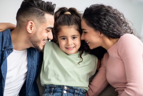 Parental Love. Happy Arabic Parents Cuddling Their Cute Little Daughter At Home